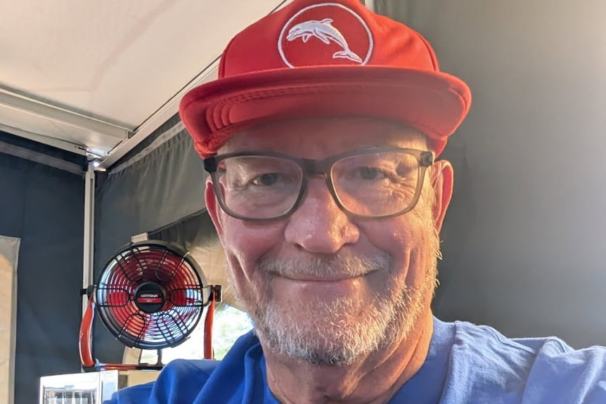 Man in his 60s with red cap and glasses smiling at camera. 