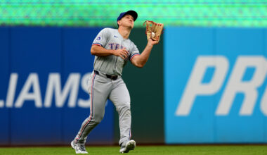 Wyatt Langford- wearning an all-grey Rangers uniform, reaches up with his glove hand (left hand) to make a catch