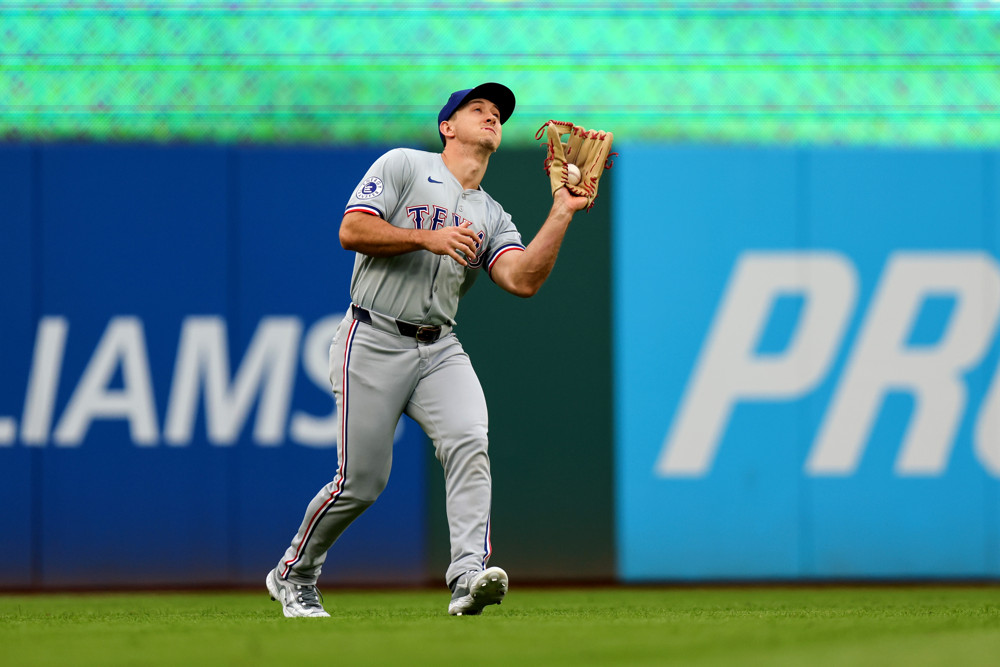 Wyatt Langford- wearning an all-grey Rangers uniform, reaches up with his glove hand (left hand) to make a catch