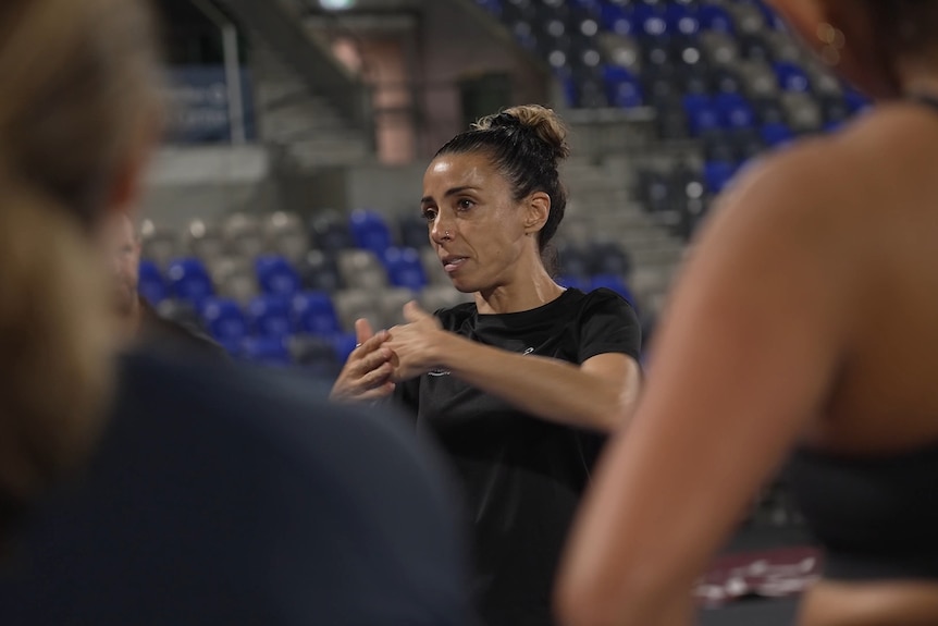 a running coach talsk to a group of women at a night time event fir women at a sydney track