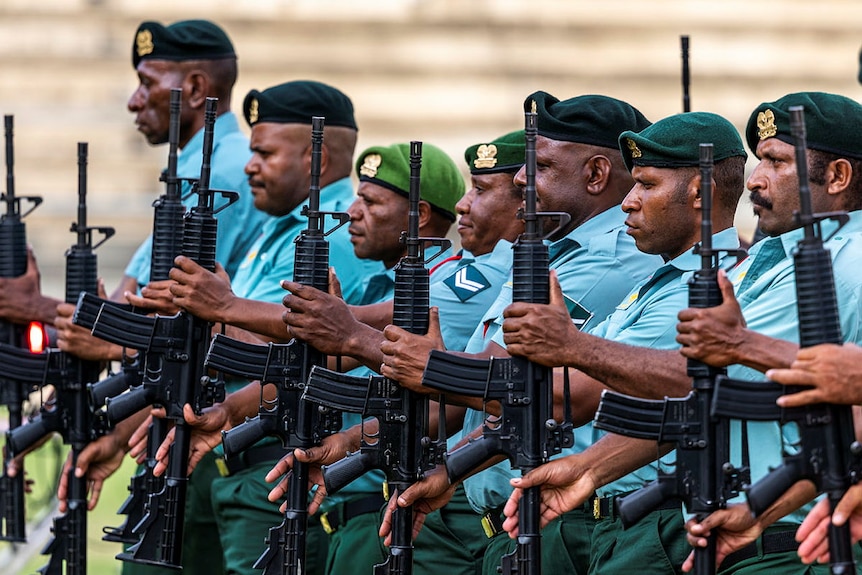 A row of PNG soldiers in blue and green uniforms, holding their guns perpindicular to the ground.