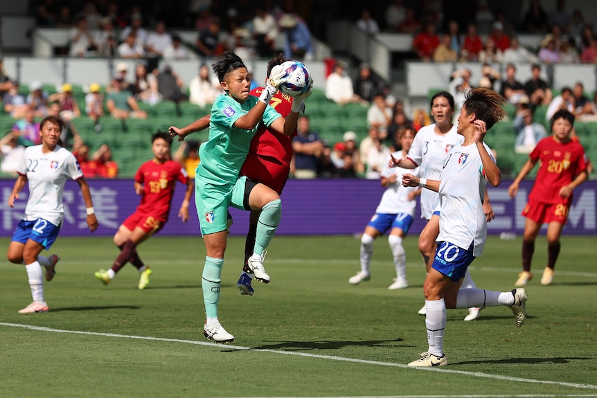 A goalkeeper in green catches a ball amongst players in red and white