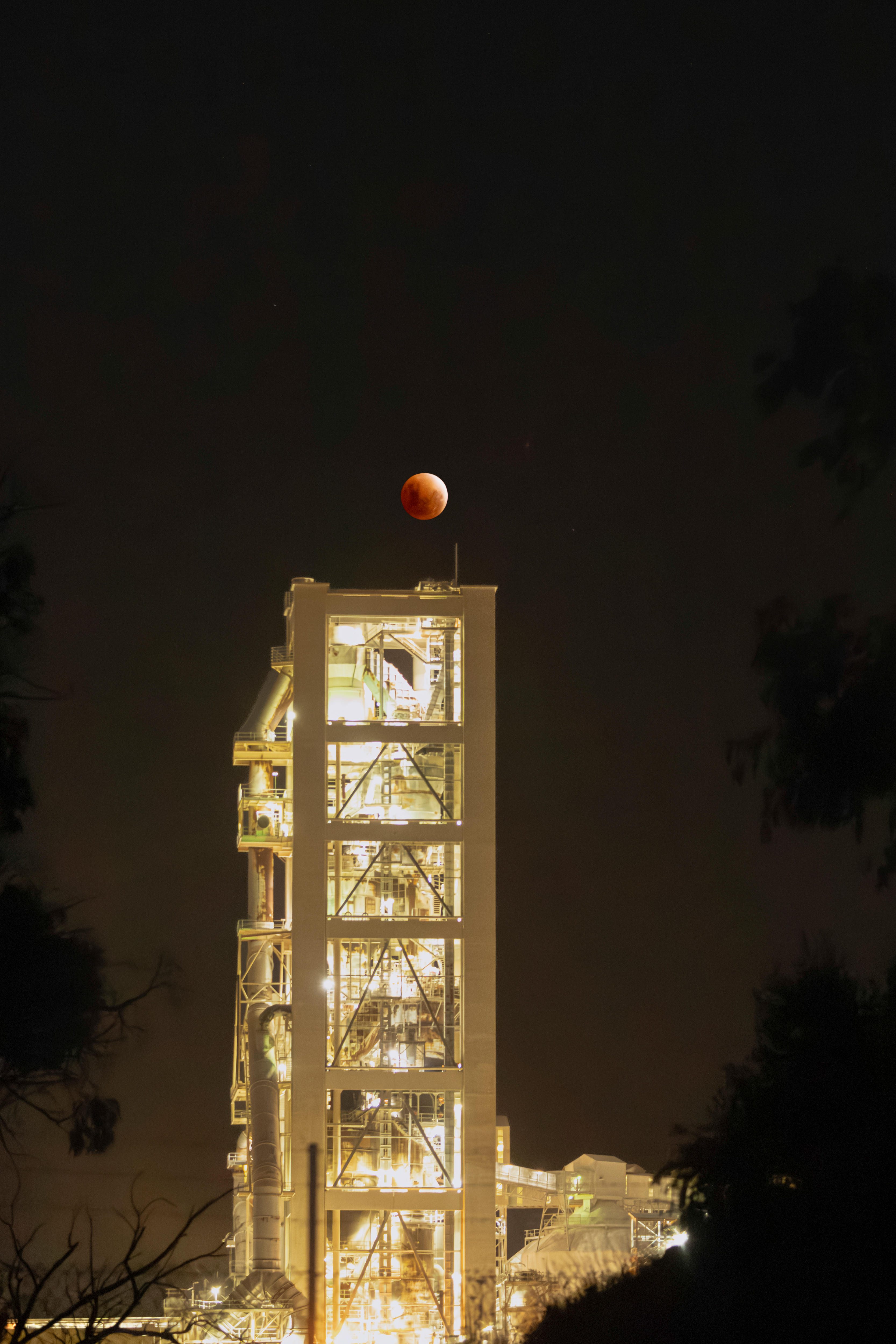 A lit up building with a bright red moon in the background in a night's sky