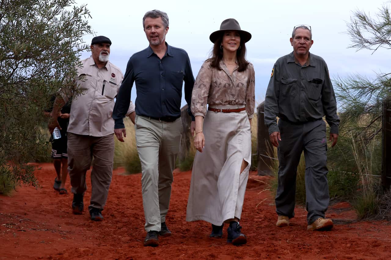 A man in a blue shirt walks with a woman wearing a hat and a white skirt. Two man are also walking beside them