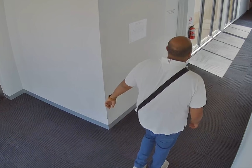 The back of a man walking through a hallway inside an apartment building.
