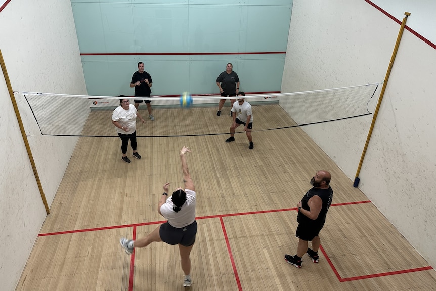 six people on a squash court with a net between them