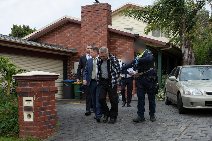 A man is led away from a home by police.