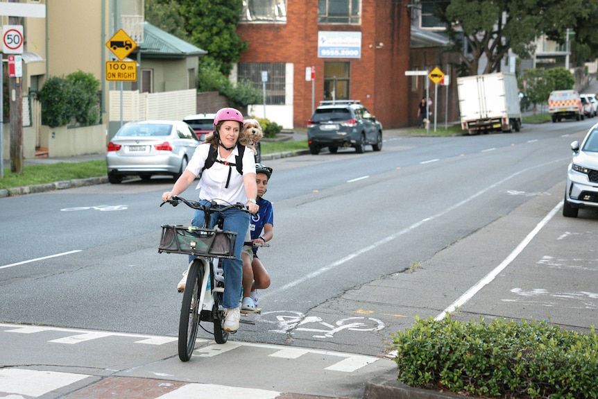 a woman rides a bike with her children on a road