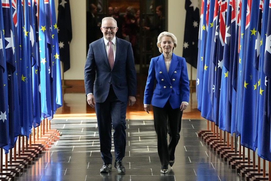 A man and a women in suits walk down a corridor lined in Australian flags.