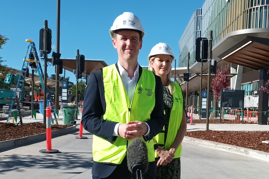 A man wearing a hard hat and high-vis vest stands at a large bus interchange with traffic lights and orange cones around it.