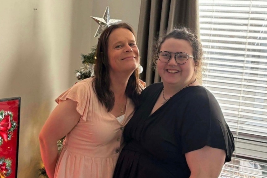 Rachel Brammer and Laura Mitchell smile together in front of Christmas tree at their home.