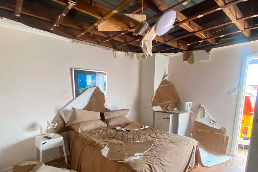 A bedroom with roof damage and debris on floor
