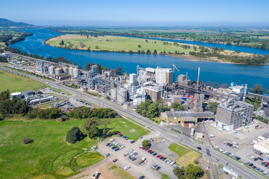 An overhead shot of a factory with grain silos between and river and a road.