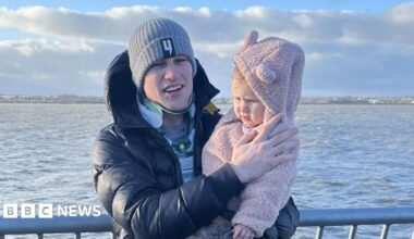 Liam McCracken, who is standing up and holding his daughter, is still wearing a neck brace as they pose for the photograph along the coast.