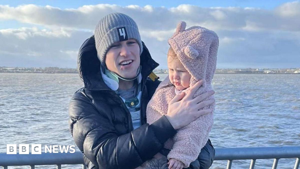 Liam McCracken, who is standing up and holding his daughter, is still wearing a neck brace as they pose for the photograph along the coast.