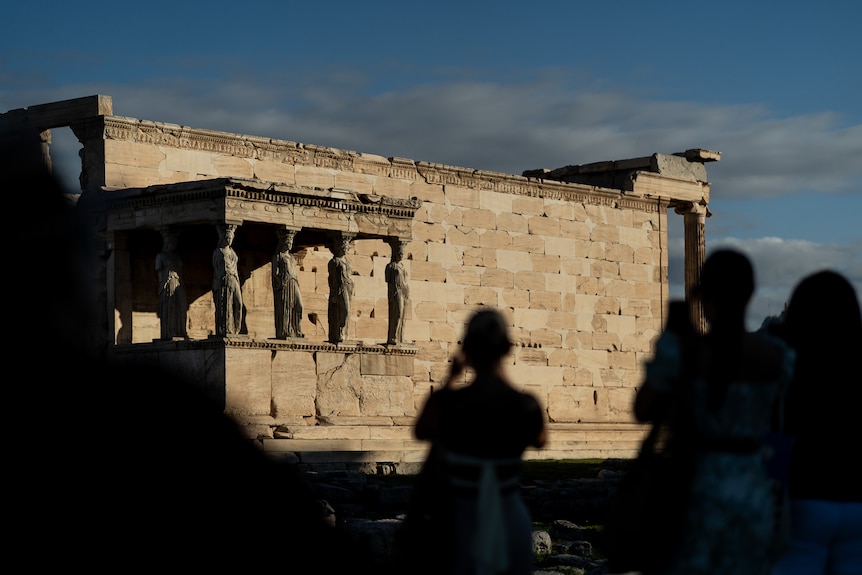 Shadows of people against the wall of the Acropolis.