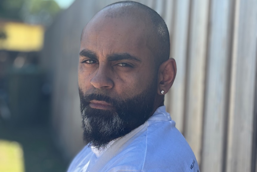 An Indigenous man with a beard near a wooden fence.