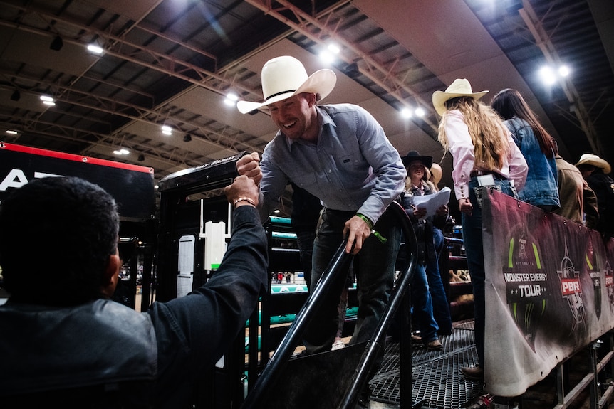 A man in a cowboy hat bumps first with another man. 
