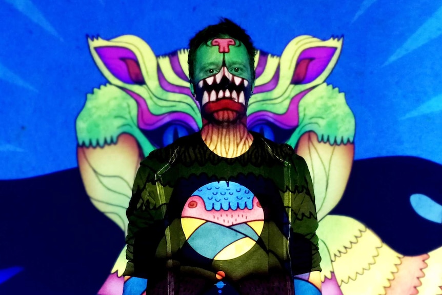 A man has a number of colourful patterns an abstract designs projected onto him.