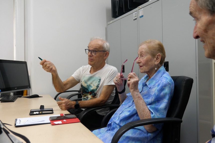 a man gestures forward while sitting next to two elderly people