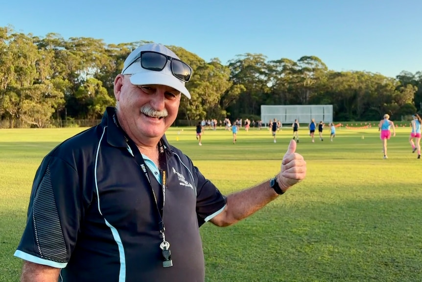 Tony Doherty smiles with a thumb up as runners train behind him.