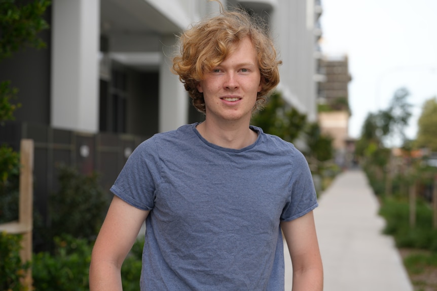Mr Nolles standing outside an apartment block with his hands on his hips while smiling at the camera as the wind blows his hair.