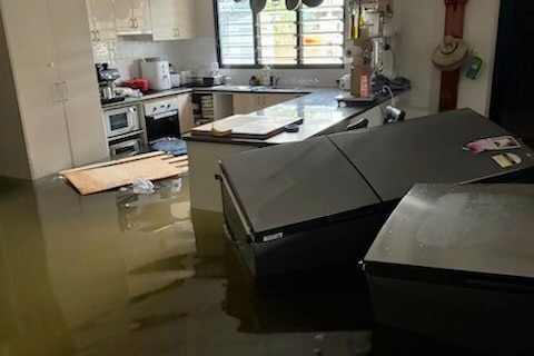 A kitchen is filled with water and a fridge floats on its side