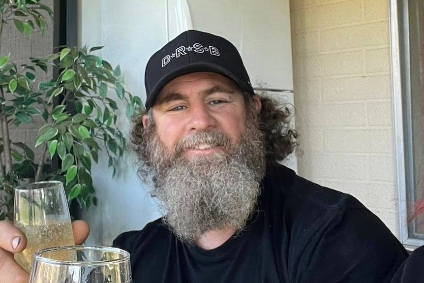 Darran Hyman man with beard and hat holds drink and smiles