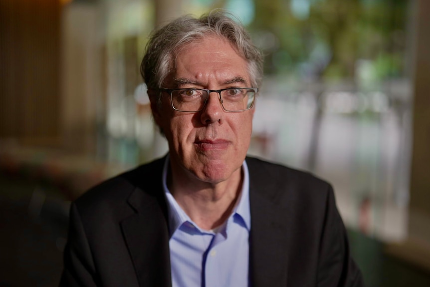 A man in glasses as suit looks at camera.