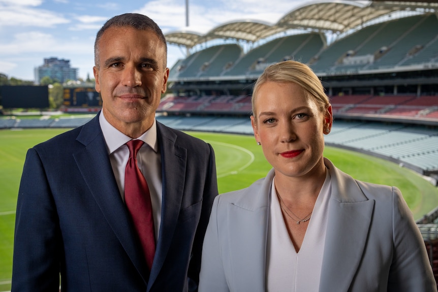 Peter Malinauskas and Ashton Hurn stand together in footy stands of an oval
