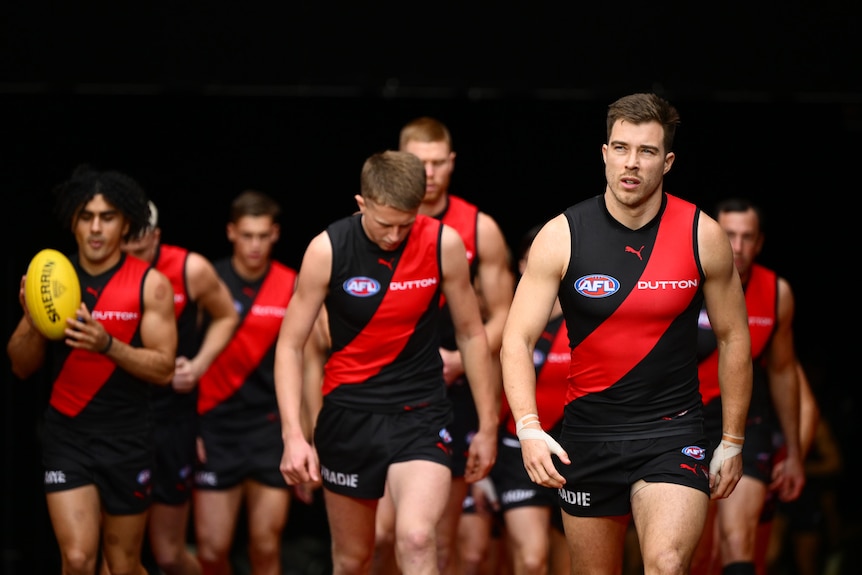 Zach Merrett leads Essendon players onto the ground.