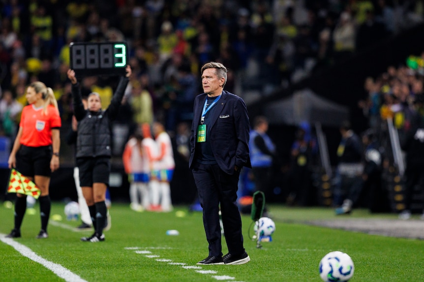 An older man stands on the side of a football field.