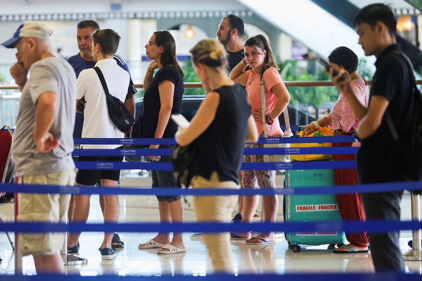 People stand in queues inside an airport, some with luggage. 