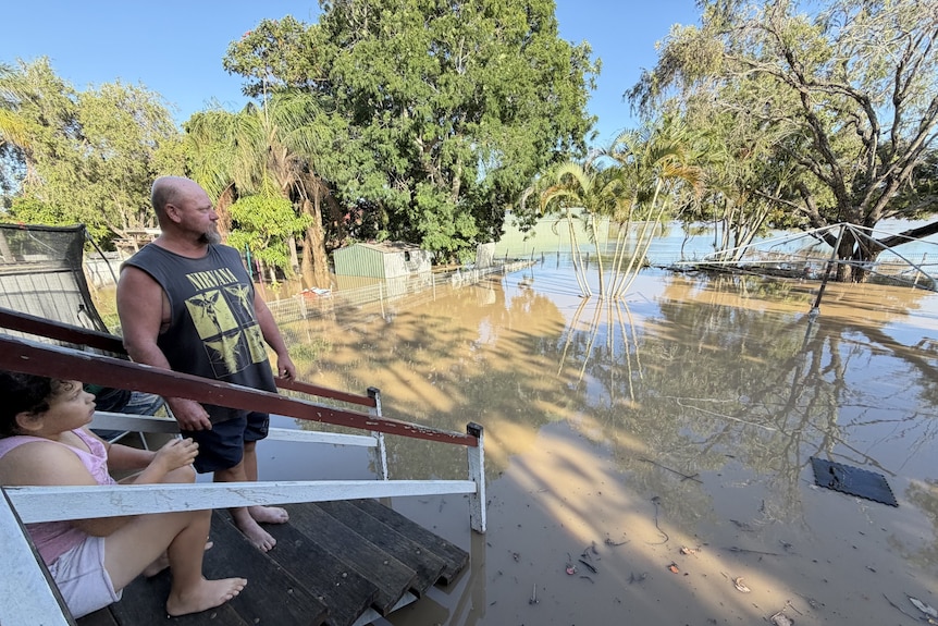 man and child on staircase leading into a flooded backyard filled with brown water