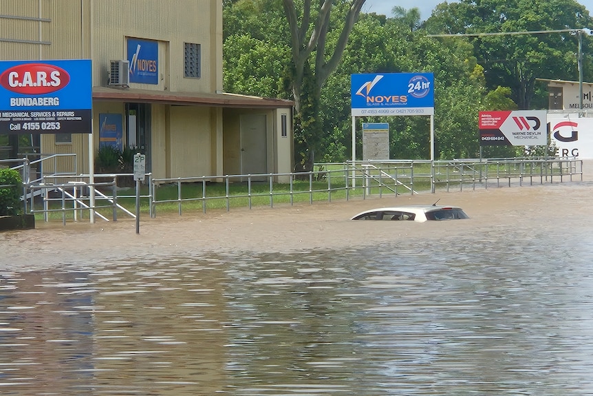 A car underwater up to its roof in front of a business.