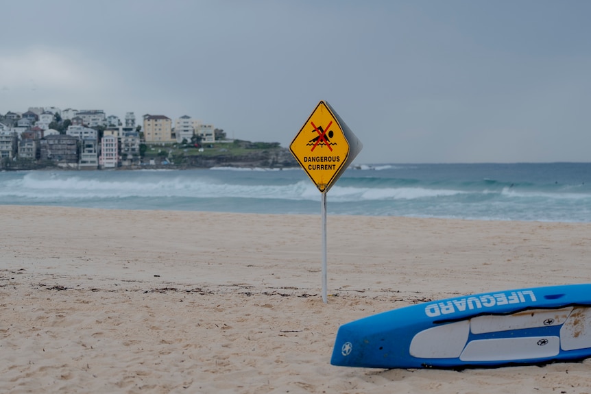 A lifeguard board on its side next to a sign with an x over someone swimming with text which reads 'dangerous current'.