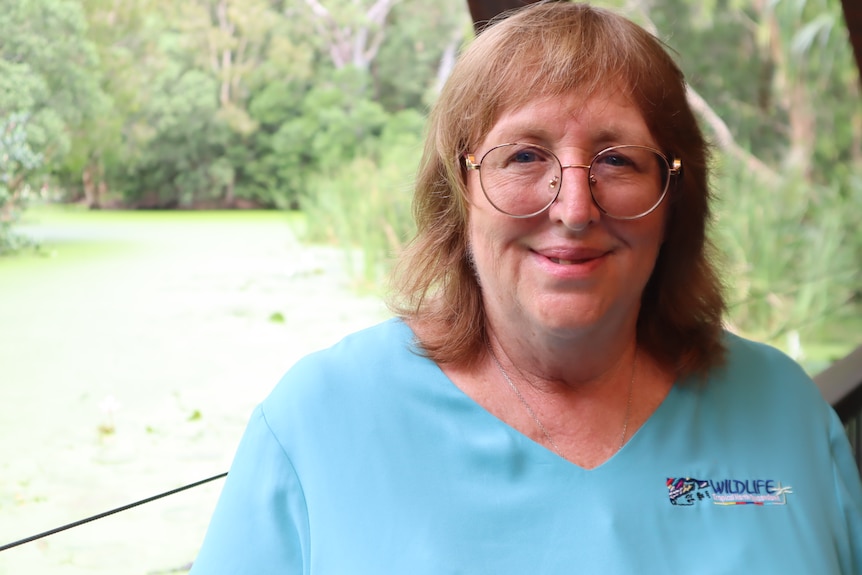 A woman in a blue shirt standing in front of a lagoon as part of a crocodile tourism farm.
