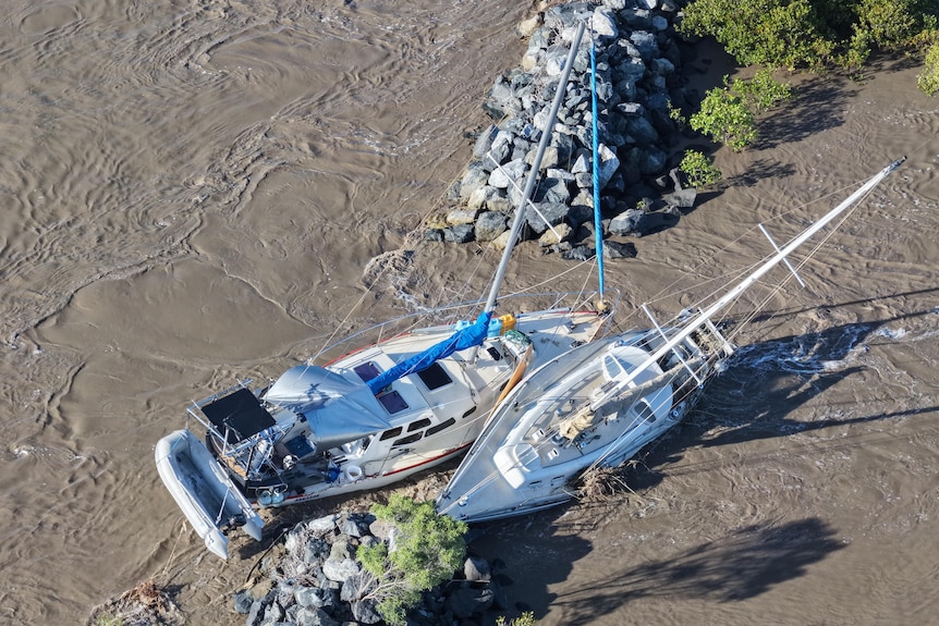 two yachts caught between rockwalls and mirky brown water