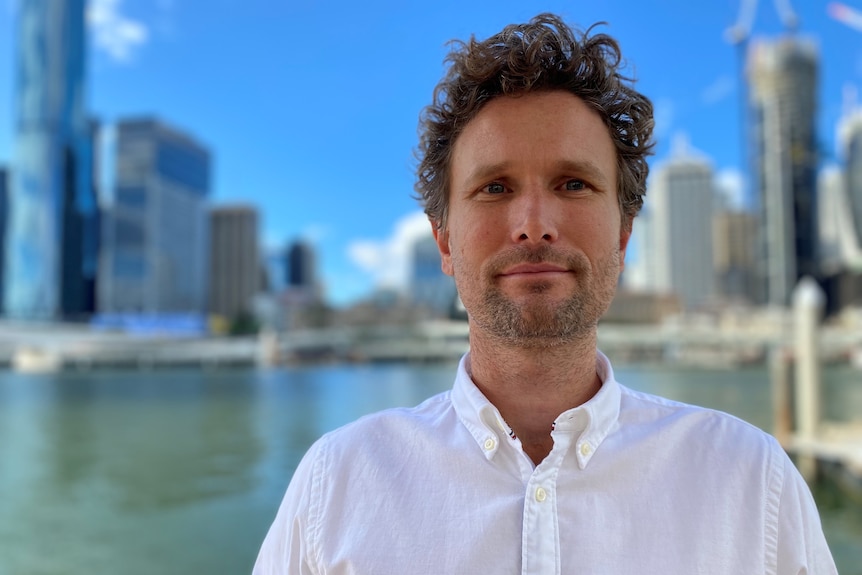 A man in a collared white shirt stands in front of the Sydney CBD skyline.