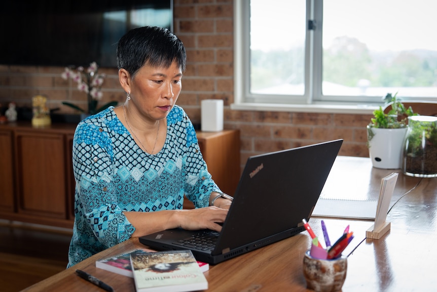 A woman in a blue shirt sitting at a table while typing on her computer