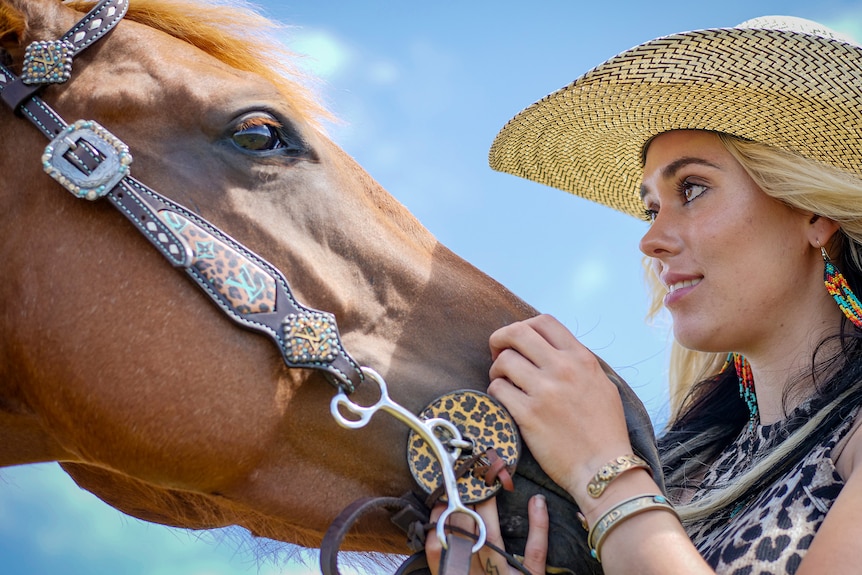 A woman scratches the nose of a chestnut horse