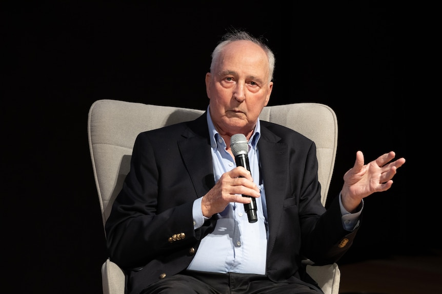Paul Keating sitting in a chair holding a microphone and speaking. 
