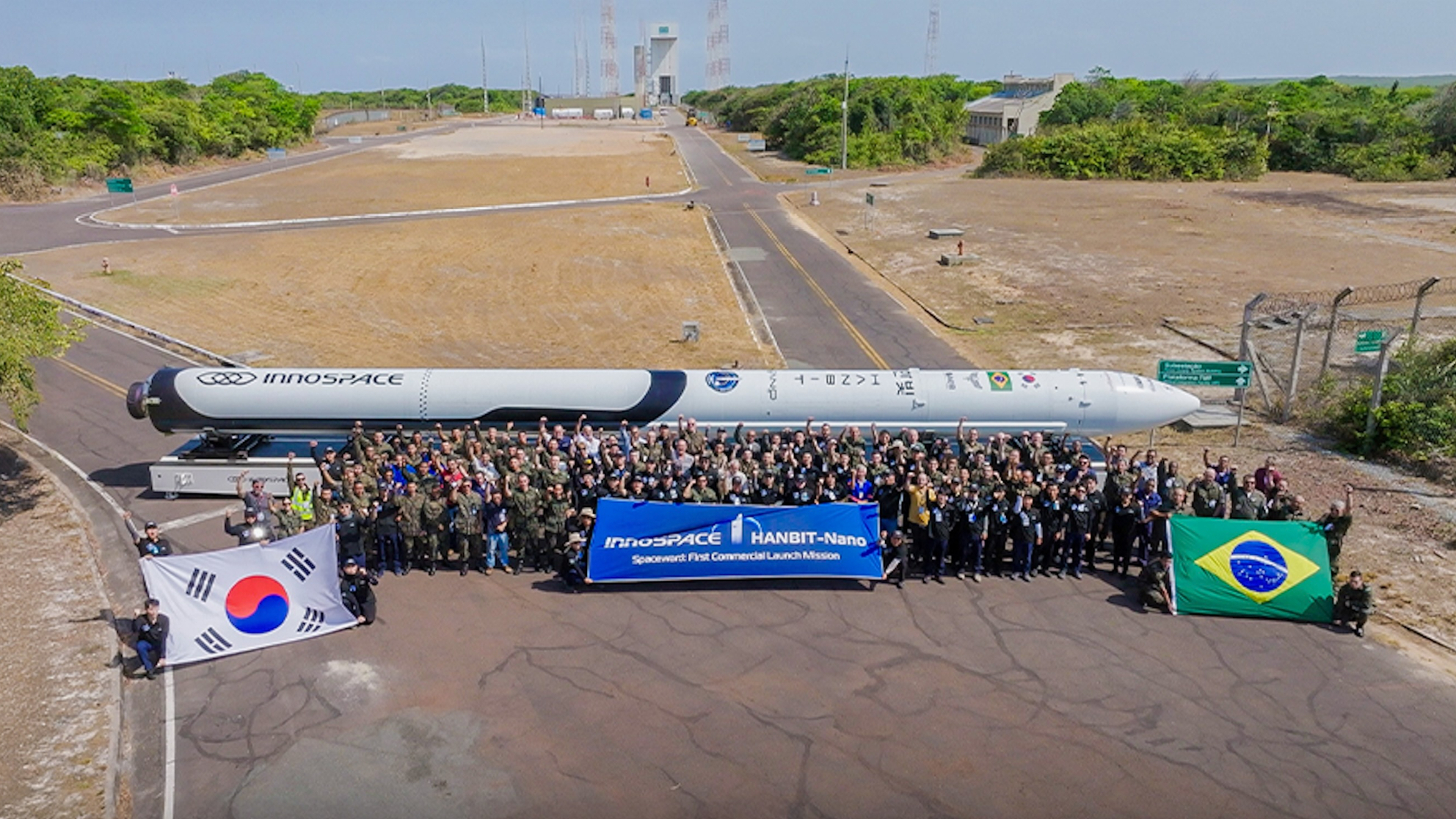 a hundred or so people stand around a white rocket, which is arrayed horizontally on the ground