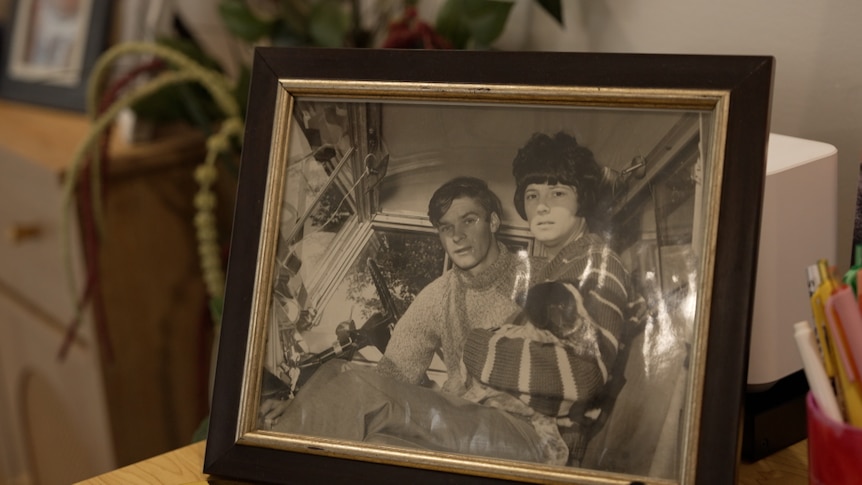 A black and white photograph featuring a man and woman in a vehicle in a black photo frame with gold trim