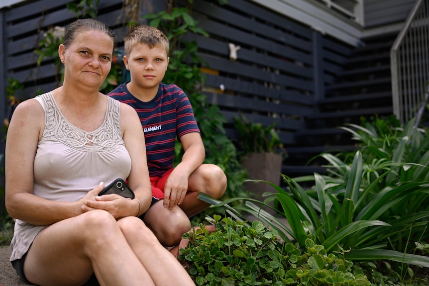 A woman and a boy sit in a garden.