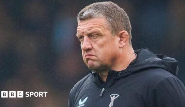 Toby Booth looks on unsmiling wearing a black hooded Harlequins training top