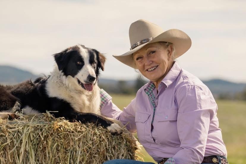 A black and white border collie and a woman in a pink shirt smiling at the camera.