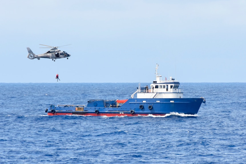 A helicopter flies above a ship in the ocean suspected of carrying drugs.