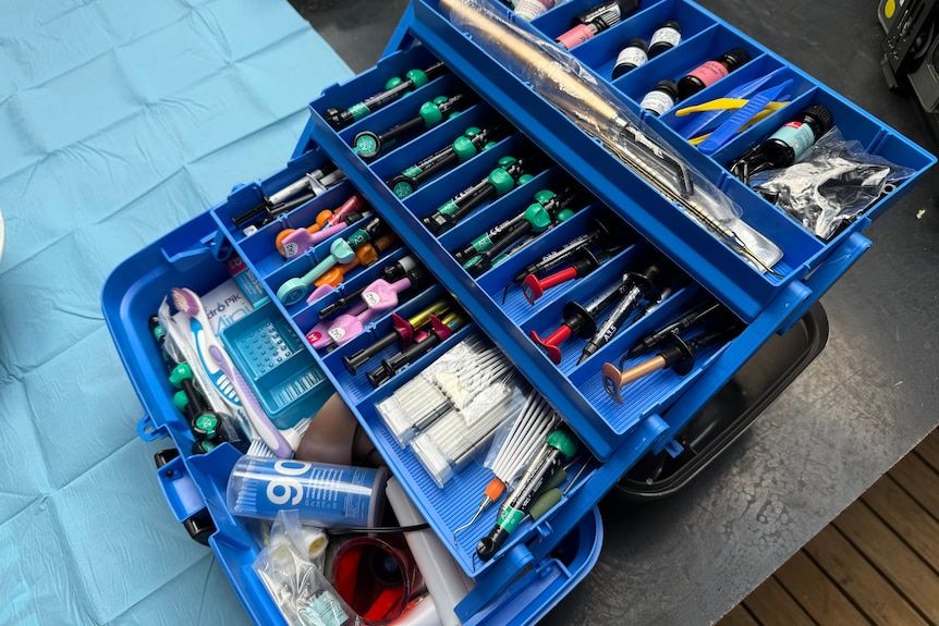 A photo of a blue supply box, with a number of dental tools in draws, displayed on a table.