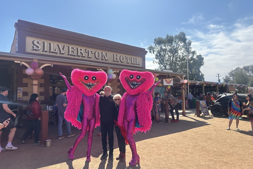 Two people in black stand with two others dressed in pink and masks outside Silverton pub.